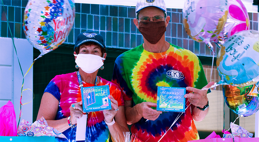 Man and woman in tie-dyed t-shirts hold up baby shower gifts