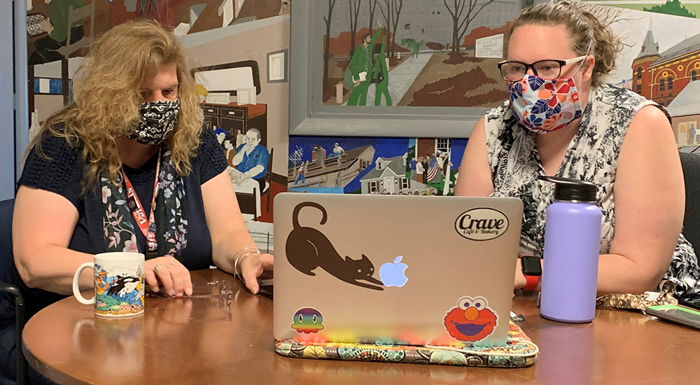 Two ladies in masks at computer on table perform peer specialist duties
