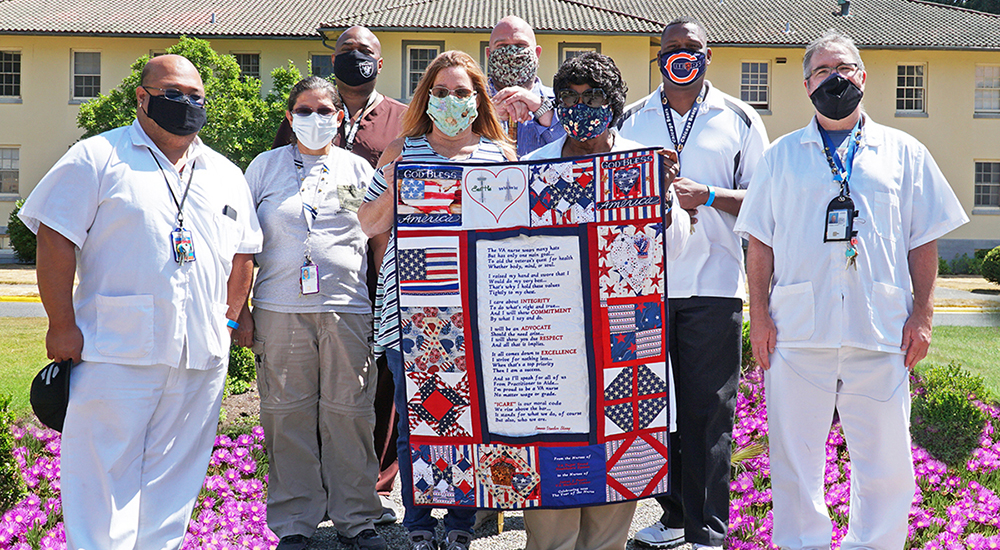 Large group of VA employees wearing mask and presenting quilt