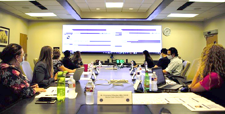 Ten people watching jumbo tele-conference screen at tele-townhall