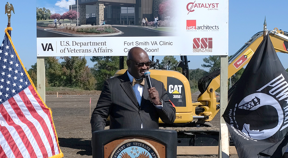 Man speaking with microphone at a podium at the Fort Smith clinic location