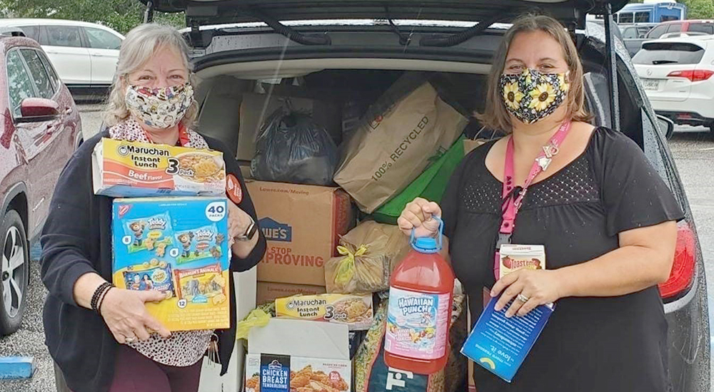 Two women in masks with donated food items