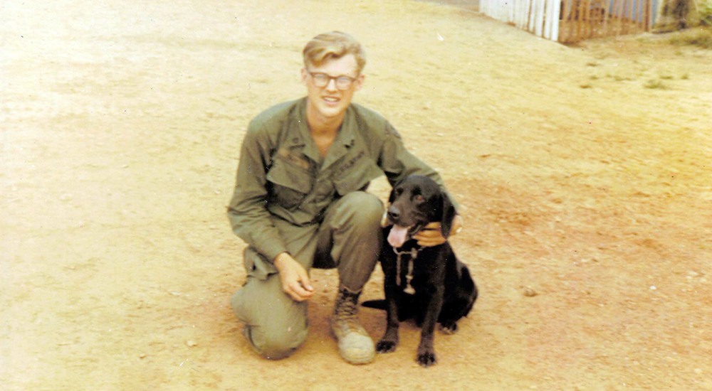 Young American Soldier in Vietnam posing with a black Labrador dog