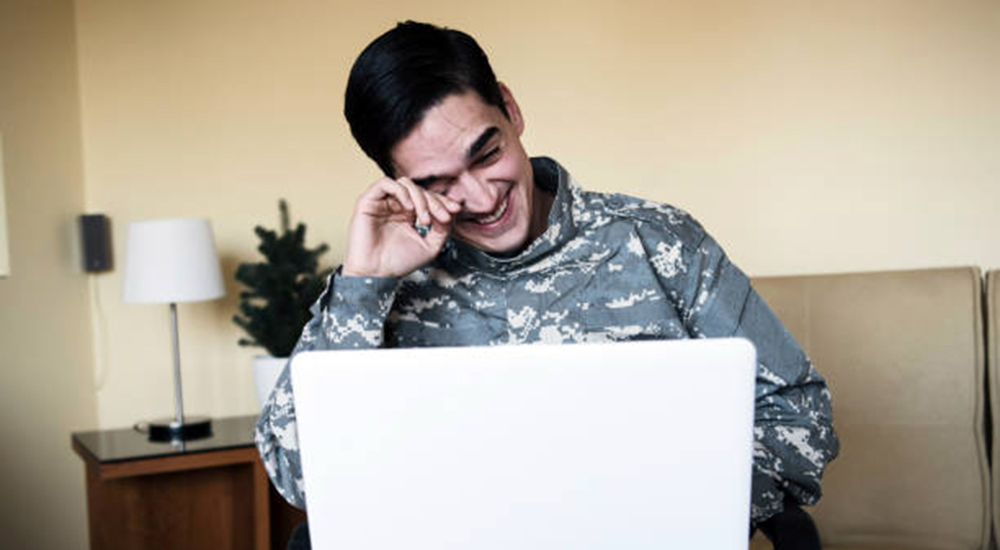 Man in uniform laughing reading laptop