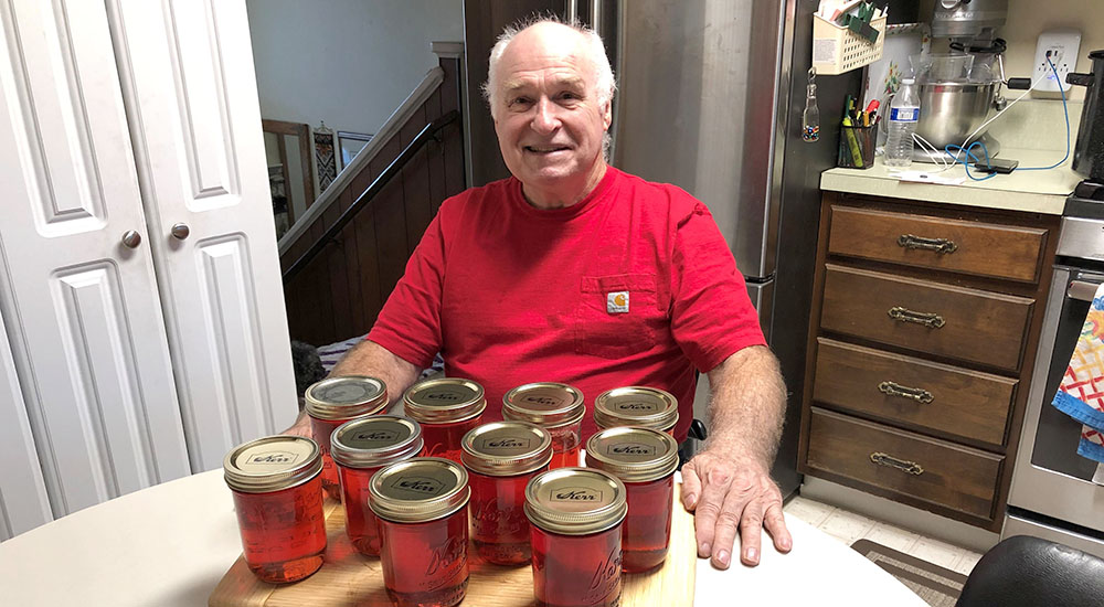 Man sitting at table with many jars of crabapple jelly