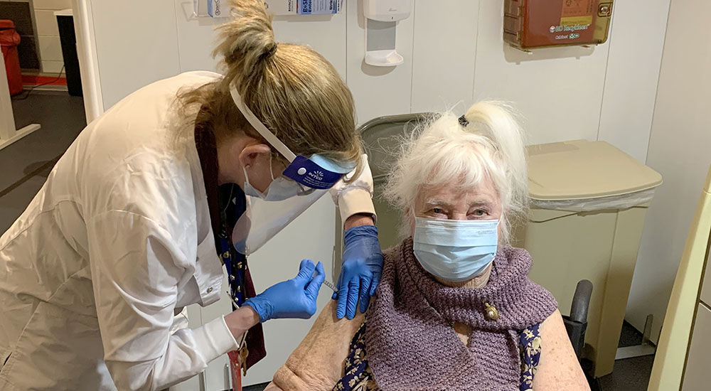 Nurse gives vaccine shot to sitting female Veteran