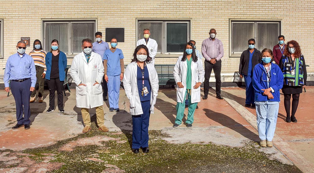 15 people wearing masks pose for photo outside hospital