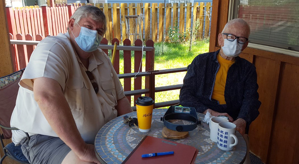 Two men, wearing masks, sitting at a table