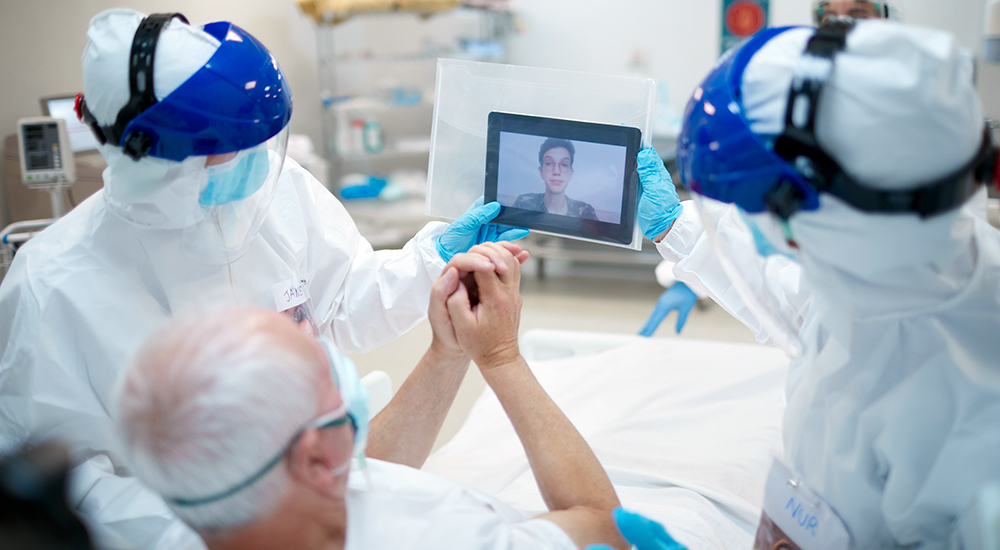Patient in bed views tablet screen held by nurses
