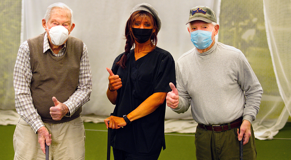 Three people wearing masks, holding golf clubs, giving thumbs up