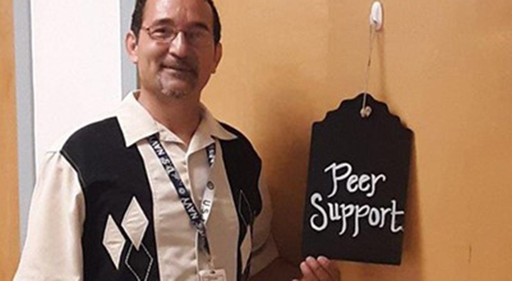 Mr. Muniz in the office holding a Peer Support sign