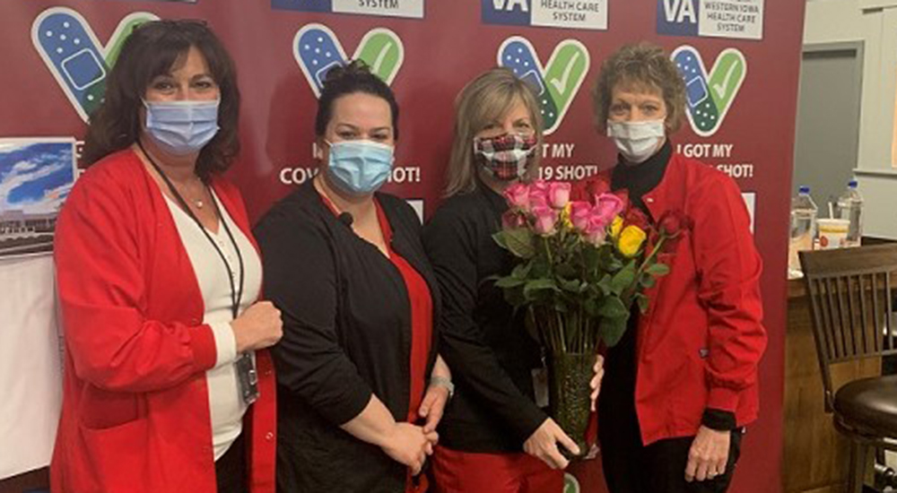 Four female nurses, wearing masks, holding roses