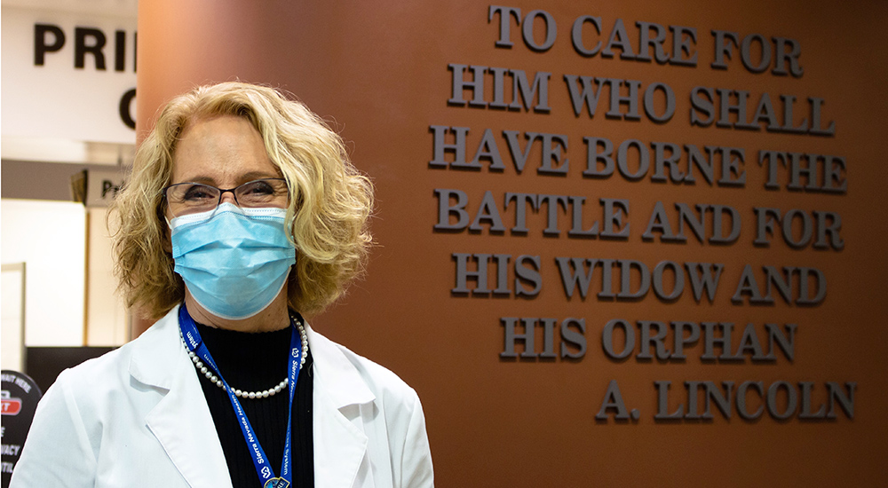 Smiling doctor in mask beside VA hospital sign