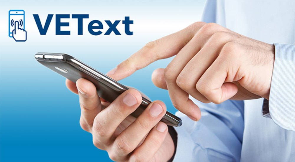 A cell phone held in a man’s hands with the word “VEText” above