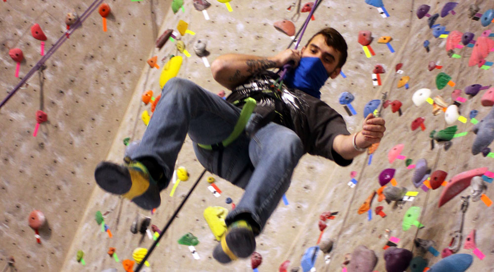 Man in harness hangs near rock climbing wall