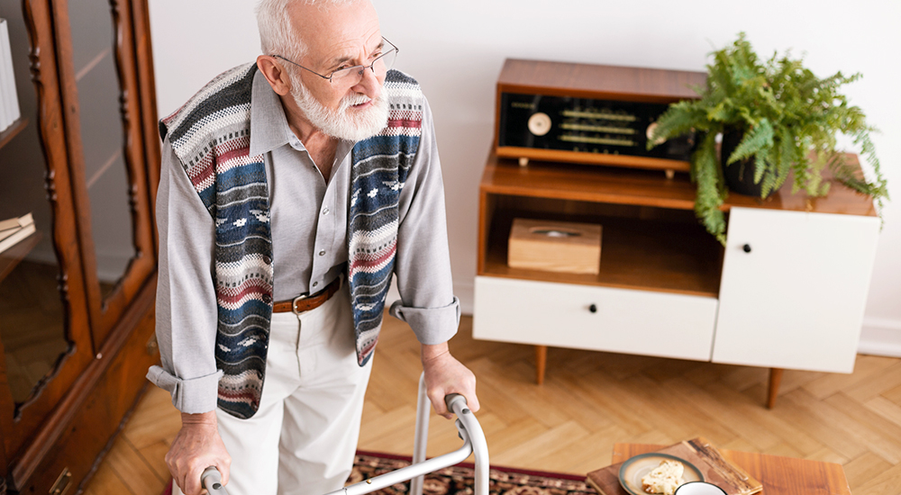 Senior handicap man walking in the apartment leaning on a walker