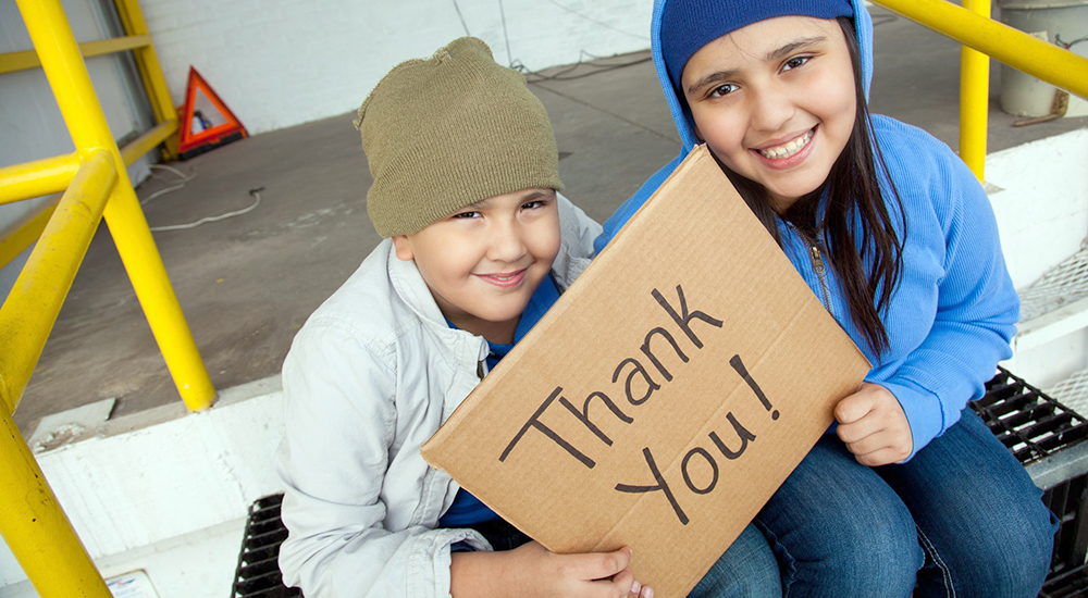Two homeless children holding Thank You sign