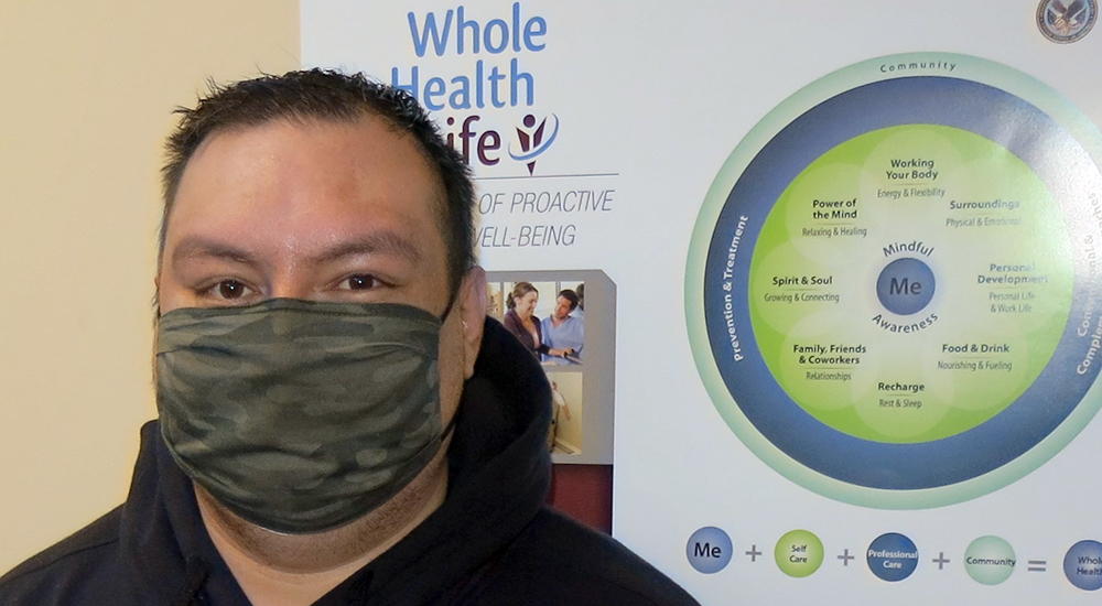 Man in mask in front of Whole Health poster