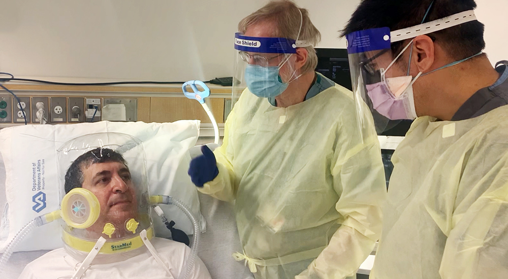 Two doctors talk to patient wearing oxygen helmet