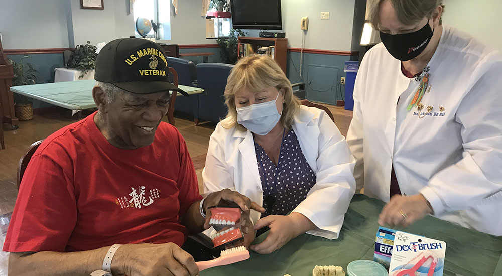 A dentist and a nurse demonstrate proper brushing to a Veteran