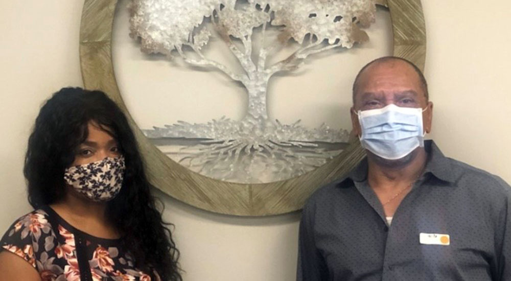 Man and woman in masks pose in front of tree picture