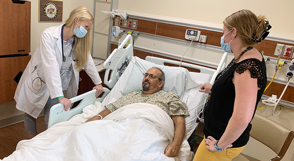 Doctor and spouse talk with man in hospital bed about immunotherapy