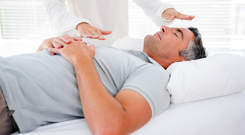 Hands held over man lying in bed