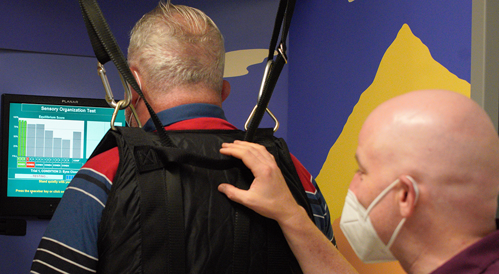 A technician helps a man find his balance while wearing a halter