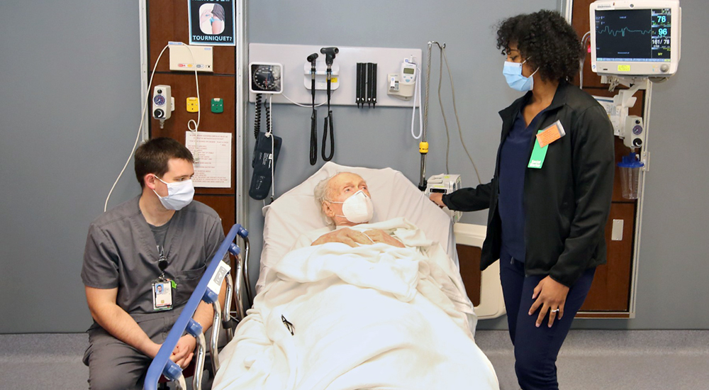 Nurse and social worker talk with elderly GERI-VET patient in ER bed