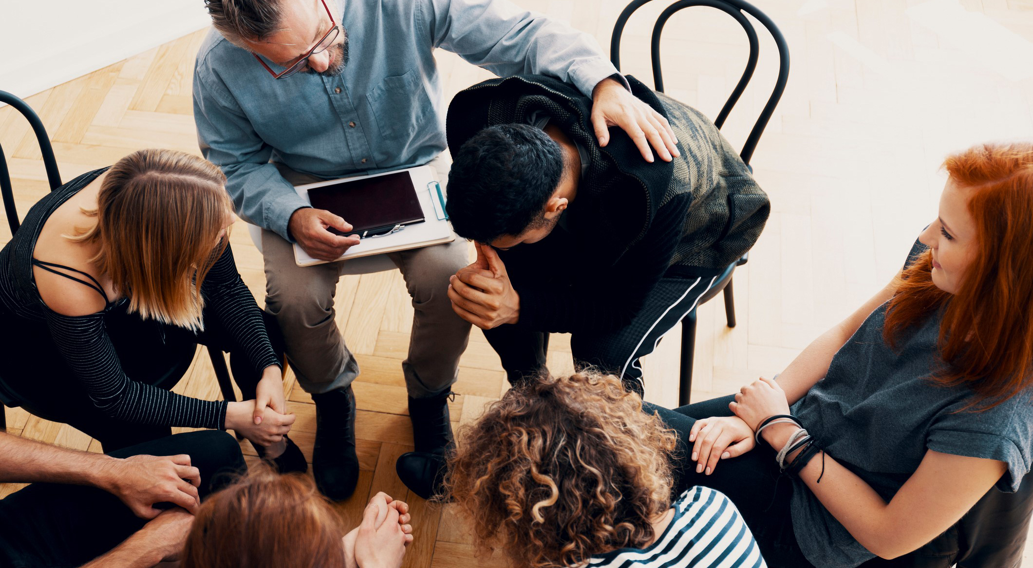 A group of people console a young man in alcohol and drug therapy