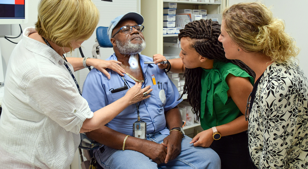 Three VA clinicians inspect a Veteran’s throat cancer procedure