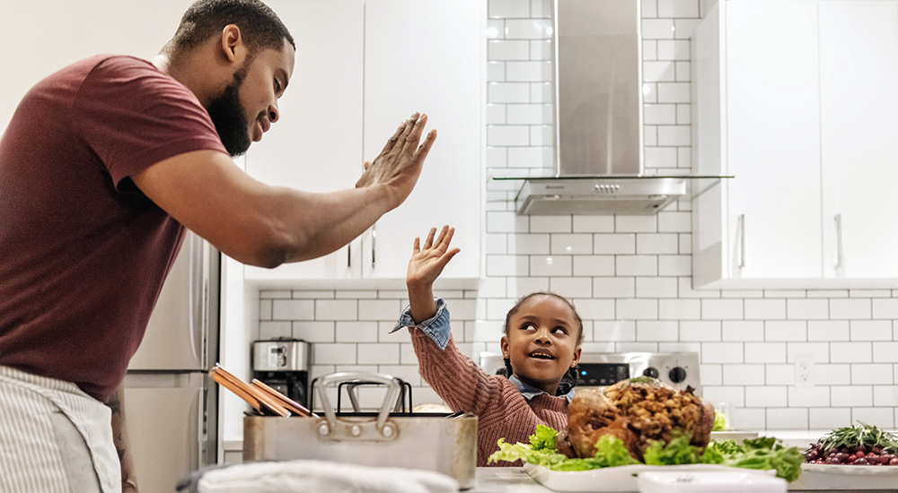 Man gives daughter high-five in the kitchen. Tina Turner song can help improve nutrition.