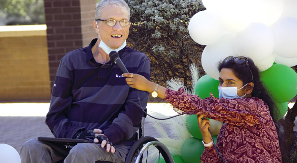 Woman holds microphone for speaker in wheelchair at spinal cord injury clinic anniversary