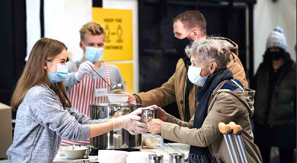 Soup kitchen volunteers serving meal to homeless couple