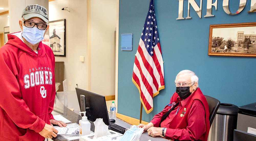 Veteran at Oklahoma VA information desk assists another Veteran with directions