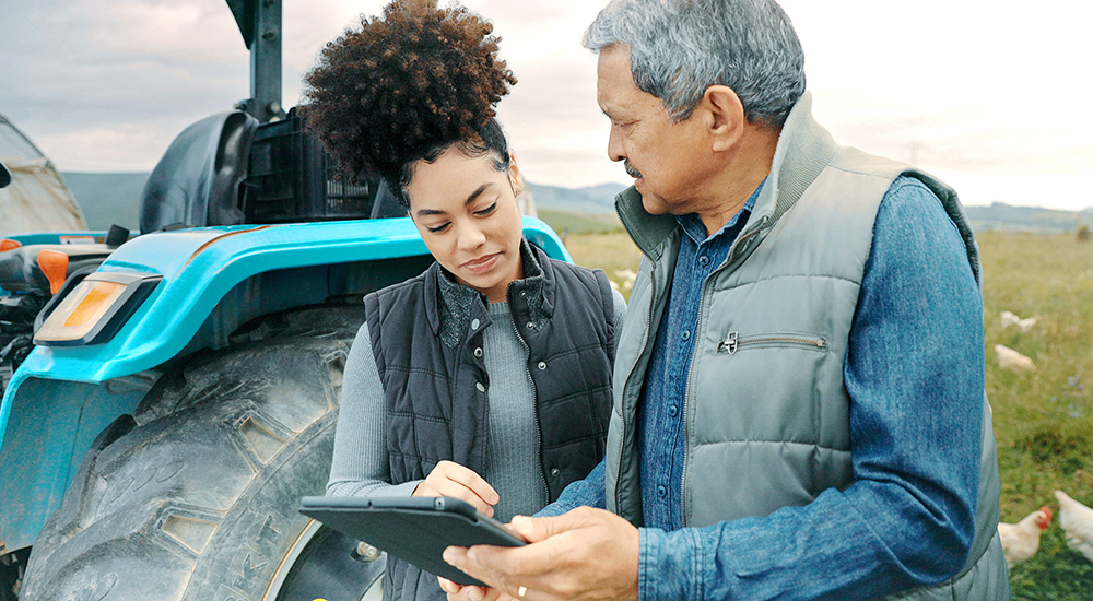 Older man and younger woman look at tablet in rural setting