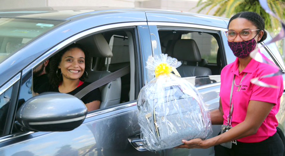 Woman hands gifts to woman in car, supporting mothers
