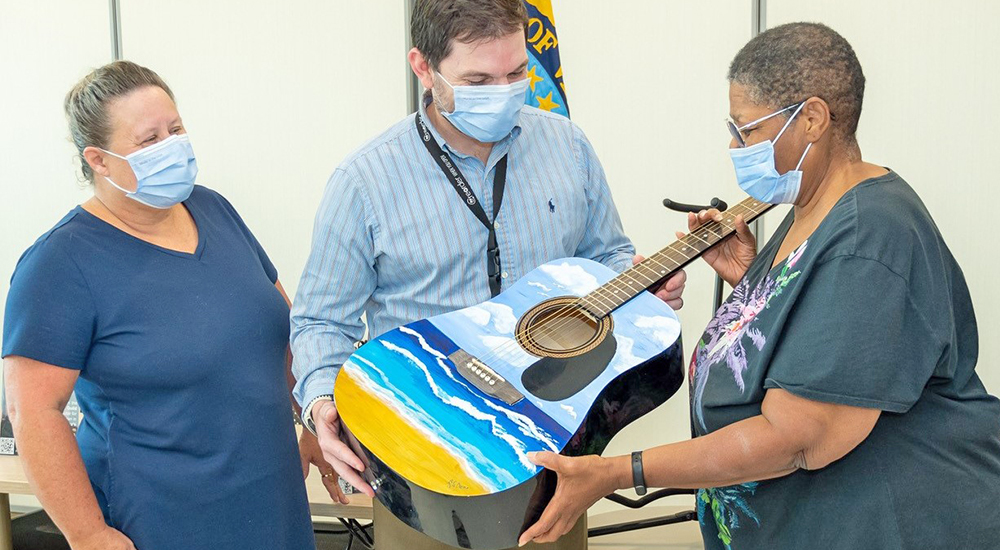 Man and woman present guitar to female Veteran for music therapy