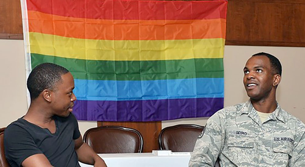 Two Veterans sit before Pride Month rainbow flag