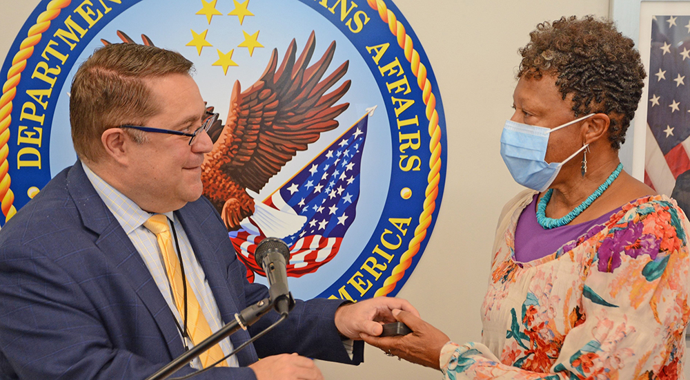 Man hands award to female Veteran at Texarkana clinic