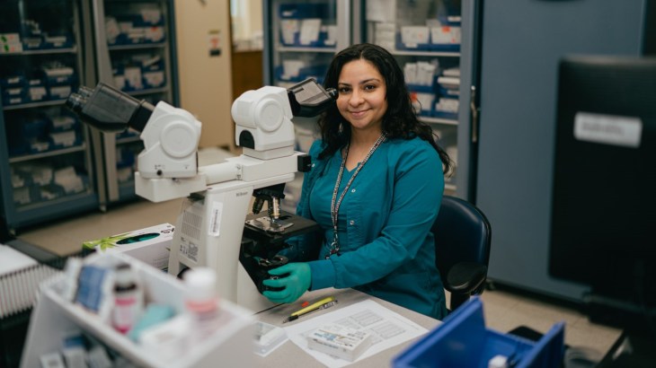 A VA employee working using a microscope to look at slides. Photo demonstrates how inclusion equals innovation at VA.