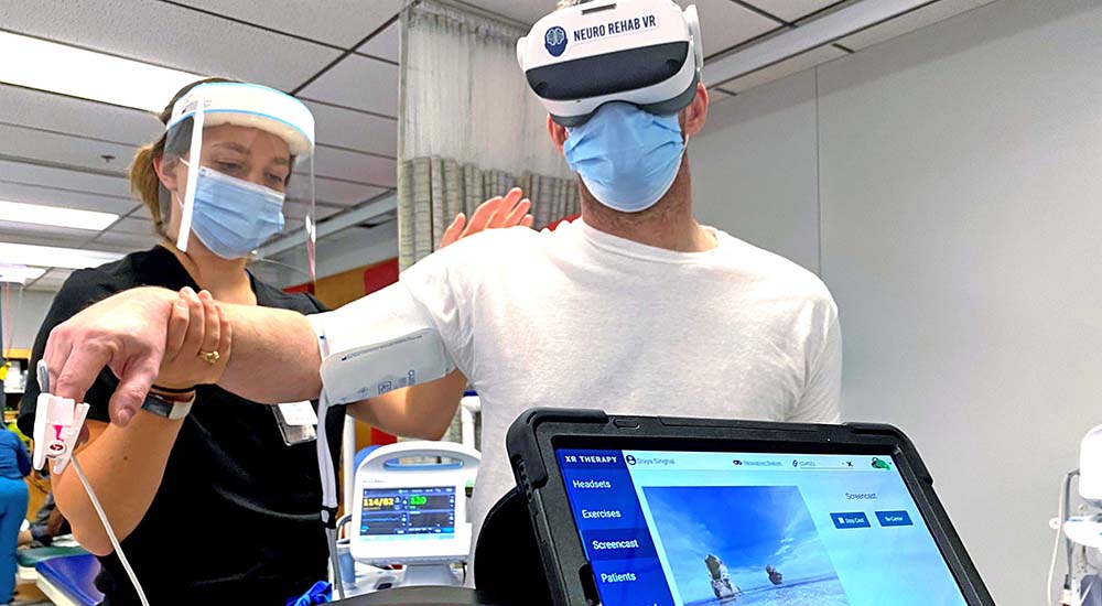 Therapist holds the arm of a Veteran wearing a virtual reality headset