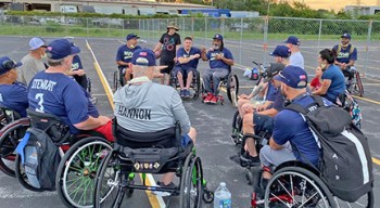 Large group of Veterans in wheelchairs on softball court