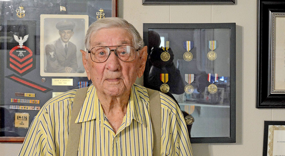 Senior Veteran in front of a wall of awards from Pacific battles