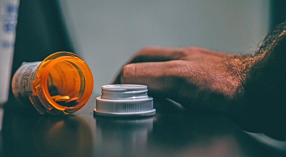 Man’s hand next to open pill bottle; medication take back days