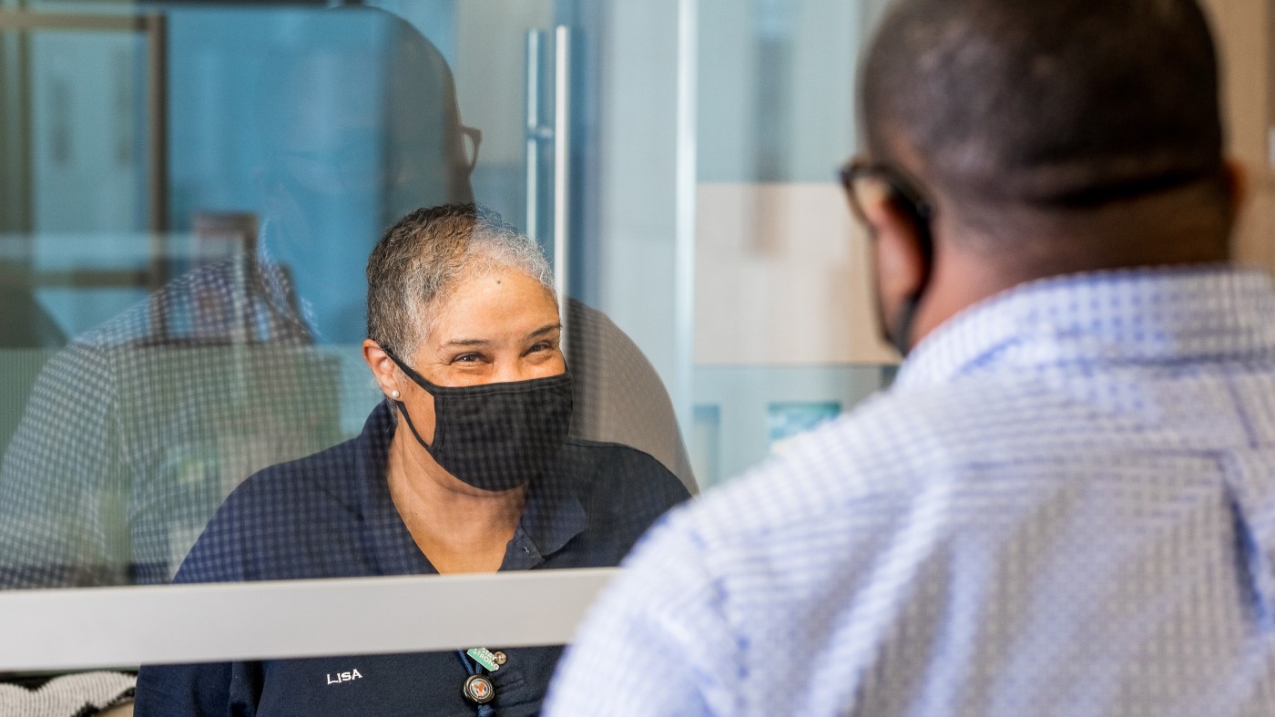 A medical support assistant wearing a mask greets a visitor at a VA facility.