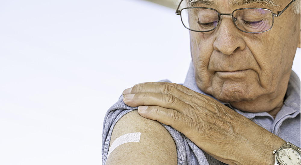 Senior man looking at bandage on his arm after flu vaccination