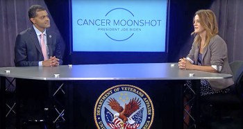 Two people at a table in front of a cancer moonshot sign