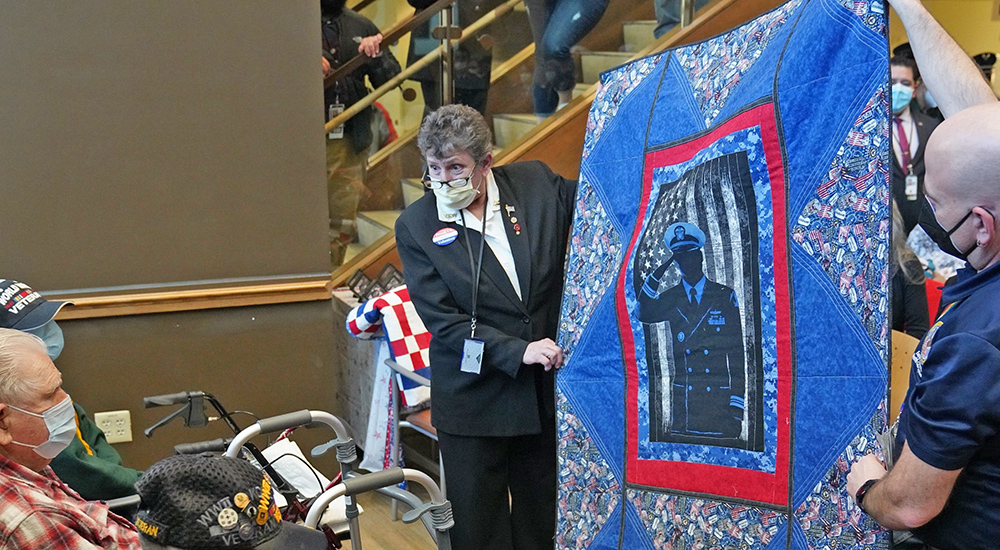 Two people showing Veteran a quilt