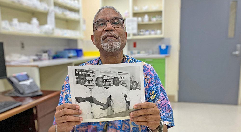 Tuskegee pharmacist holding photo of his father and VA staff